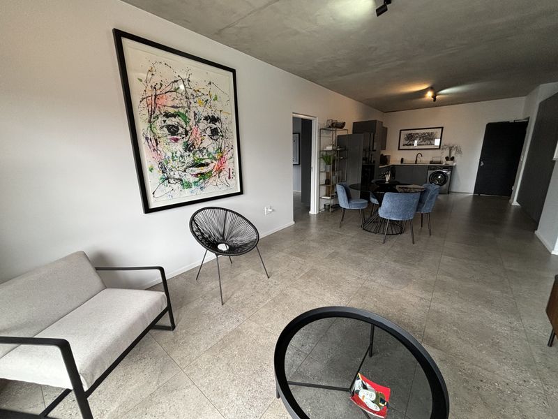 Spacious open-plan living and kitchen area featuring modern tiled floors, an exposed concrete ceiling, and a functional kitchen layout.