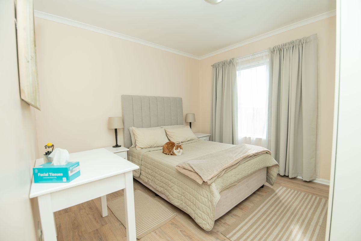 A well-maintained bedroom featuring neutral wall tones, laminate flooring, and a window with fitted curtains.