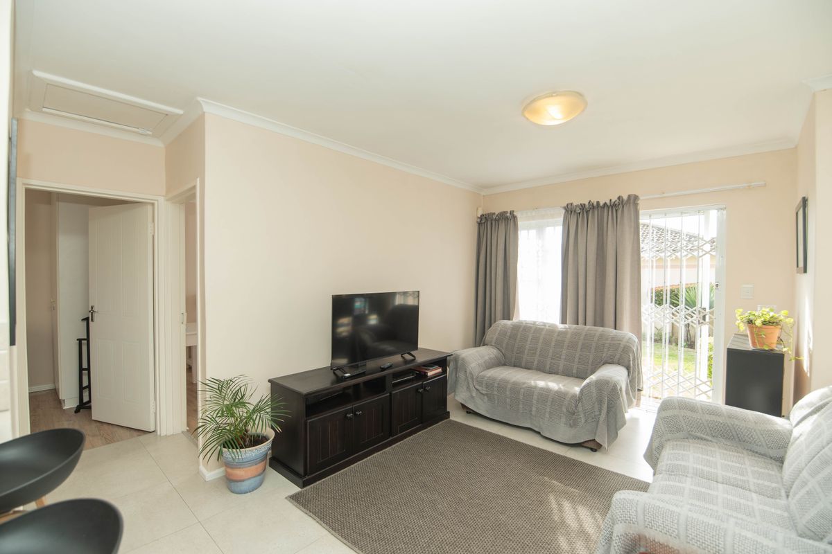 A bright living room featuring tiled flooring and a sliding door with a security gate, providing direct access to the outdoor area.