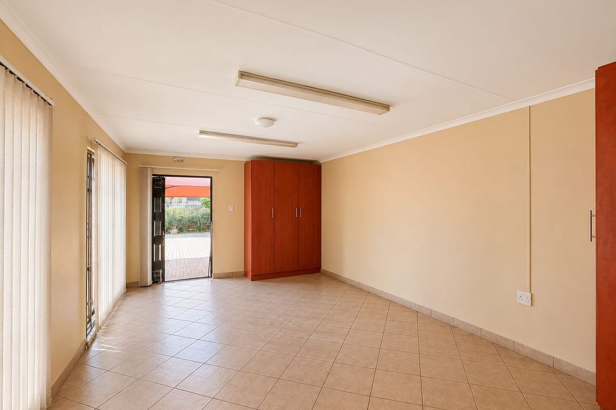 Spacious bedroom featuring neutral tiled flooring, built-in cupboards, vertical blinds, and direct access to the exterior through a security gate.