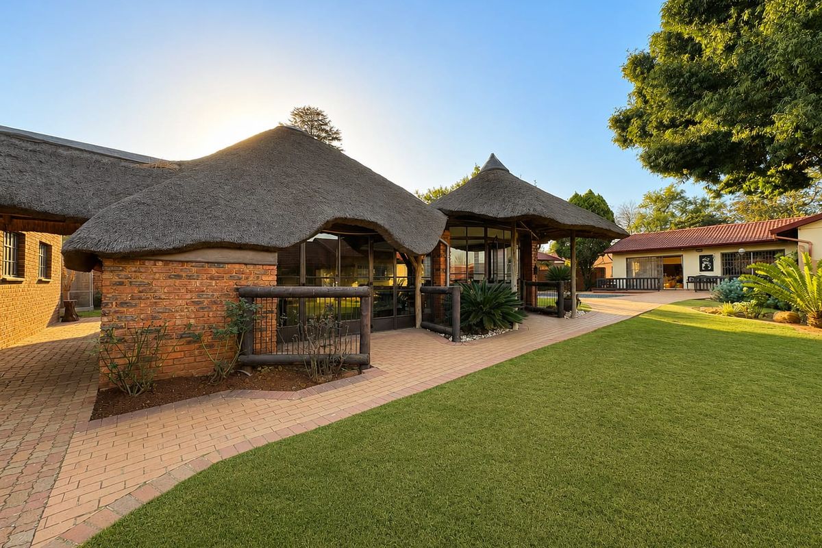 A well-maintained rear garden featuring a unique thatched roof structure, exposed brick facade, and a paved walkway leading to the outdoor living area.