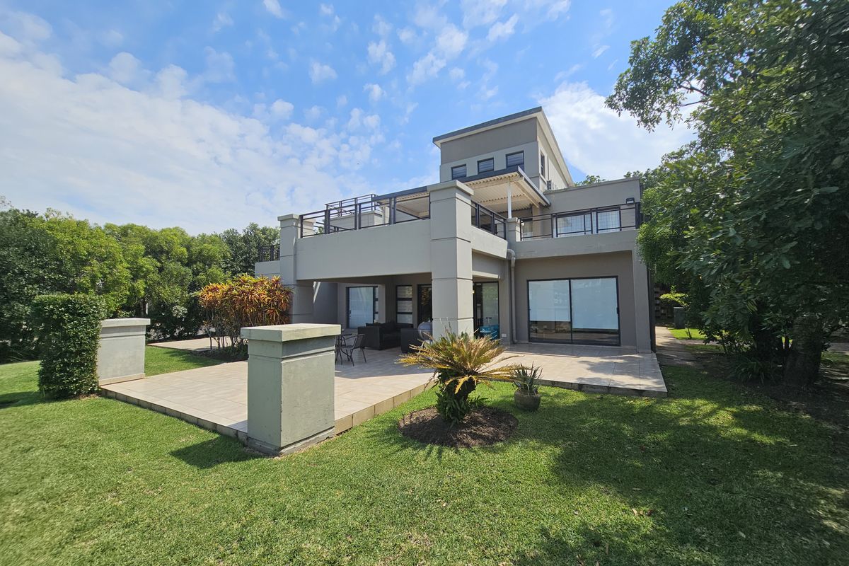 Rear view of a modern multi-level apartment building featuring a spacious tiled patio, upper-level balcony, and well-maintained landscaped garden.