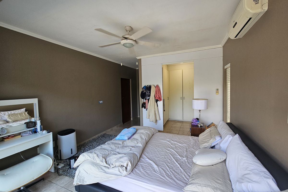 Spacious bedroom featuring tiled flooring, built-in cupboards, a ceiling fan, and a wall-mounted air conditioning unit.
