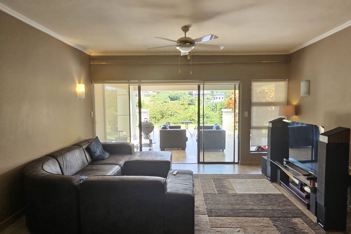 Spacious living room featuring tiled flooring, a ceiling fan, and large sliding glass doors that provide natural light and access to the outdoor patio.