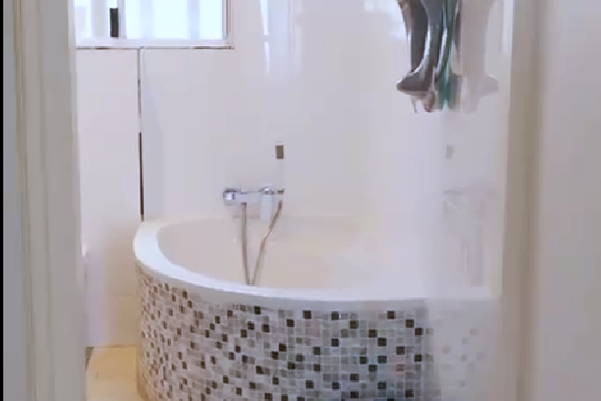 A bathroom featuring a built-in corner bathtub with a decorative mosaic tile surround, complemented by tiled walls and flooring.