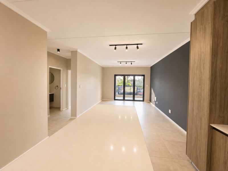 Spacious open-plan living area featuring a large stone kitchen island, modern track lighting, neutral tiled floors, and sliding doors leading to a balcony.