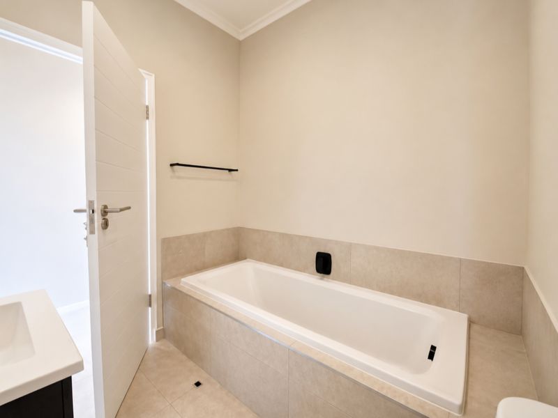 A clean, modern bathroom featuring a built-in bathtub with neutral tiling, a vanity basin, and a minimalist towel rail.