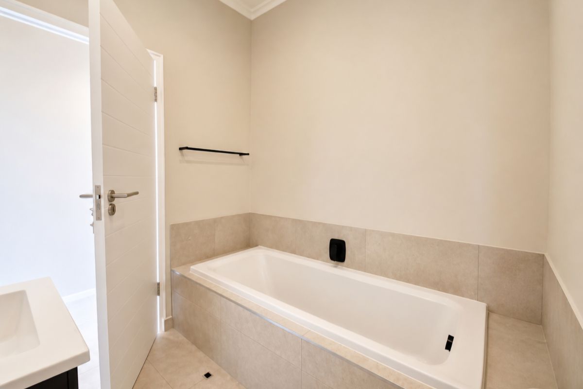 A clean, modern bathroom featuring a built-in bathtub with neutral tiling, a vanity basin, and a minimalist towel rail.