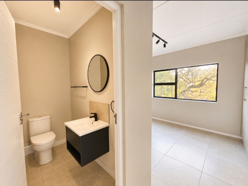 A modern, minimalist bathroom featuring a wall-mounted vanity with a black mixer tap, adjacent to a bright, tiled room with large window views.