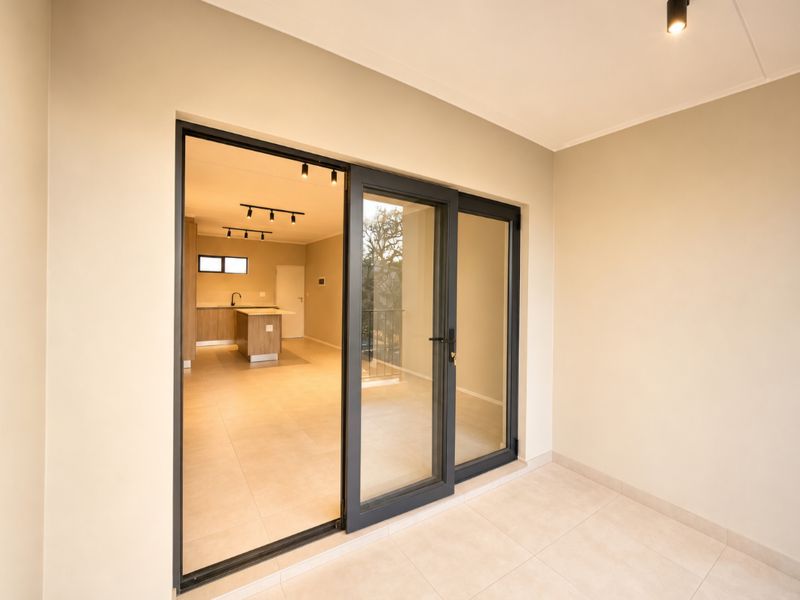 A clean, modern balcony with tiled flooring and sliding glass doors providing a view into an open-plan kitchen area.