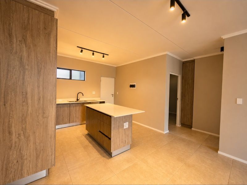 Modern kitchen featuring wood-look cabinetry, a central island with stone countertop, track lighting, and neutral tiled flooring in an open-plan layout.