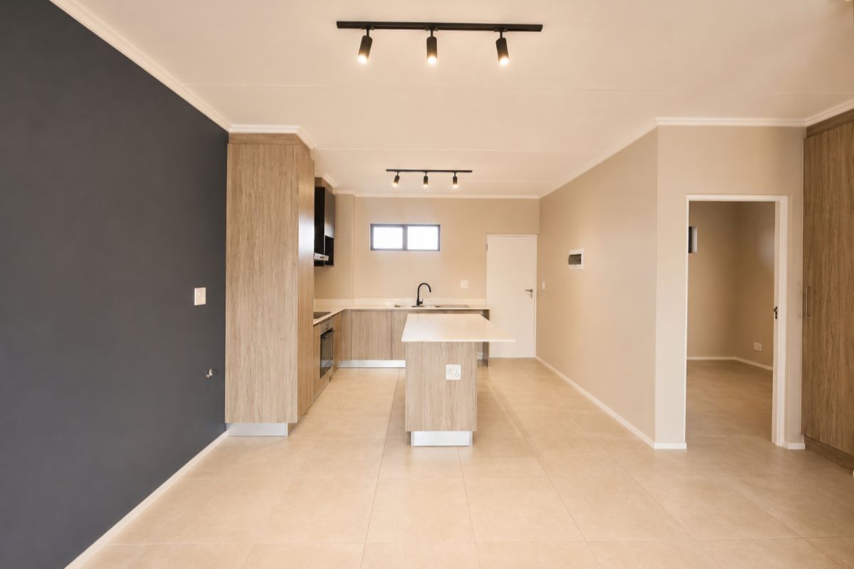 Modern, open-plan kitchen featuring light wood cabinetry, a central island, built-in oven, and neutral tiled flooring with contemporary track lighting.