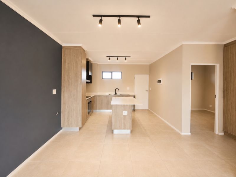 Modern, open-plan kitchen featuring light wood cabinetry, a central island, built-in oven, and neutral tiled flooring with contemporary track lighting.