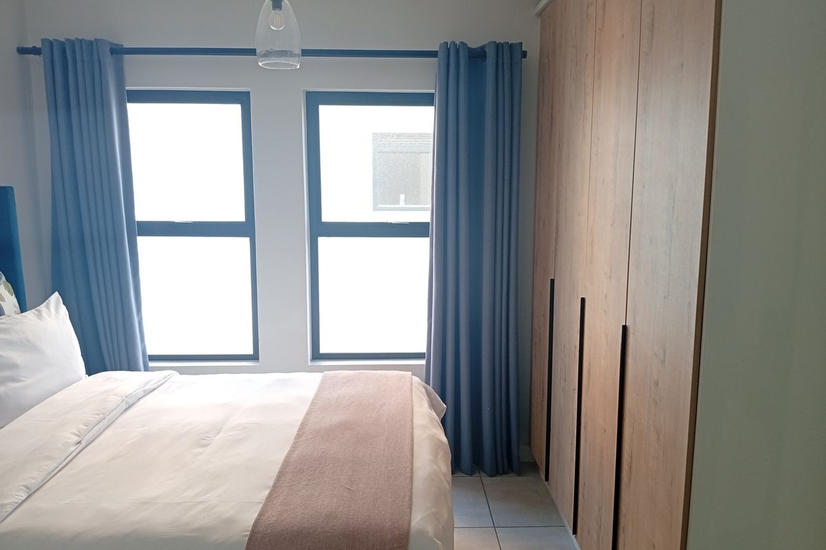 A well-maintained bedroom featuring modern built-in wardrobes, tiled flooring, and large windows that provide ample natural light.
