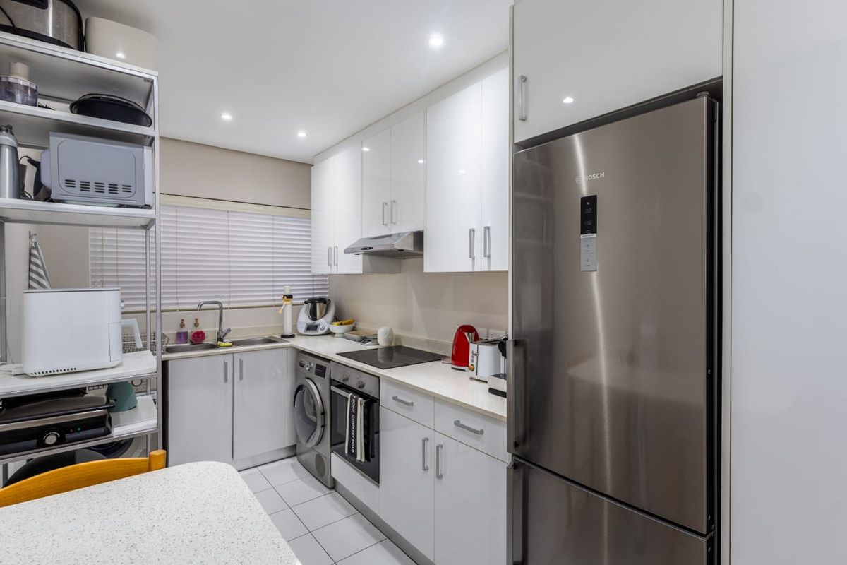 A modern, compact kitchen featuring white high-gloss cabinetry, stainless steel appliances, integrated laundry facilities, and recessed lighting.