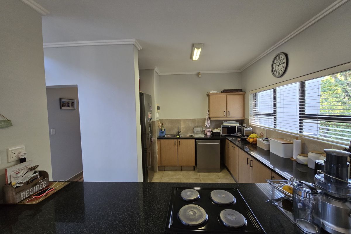 A functional kitchen featuring granite countertops, built-in wooden cabinetry, an electric hob, and a tiled backsplash with ample natural light.