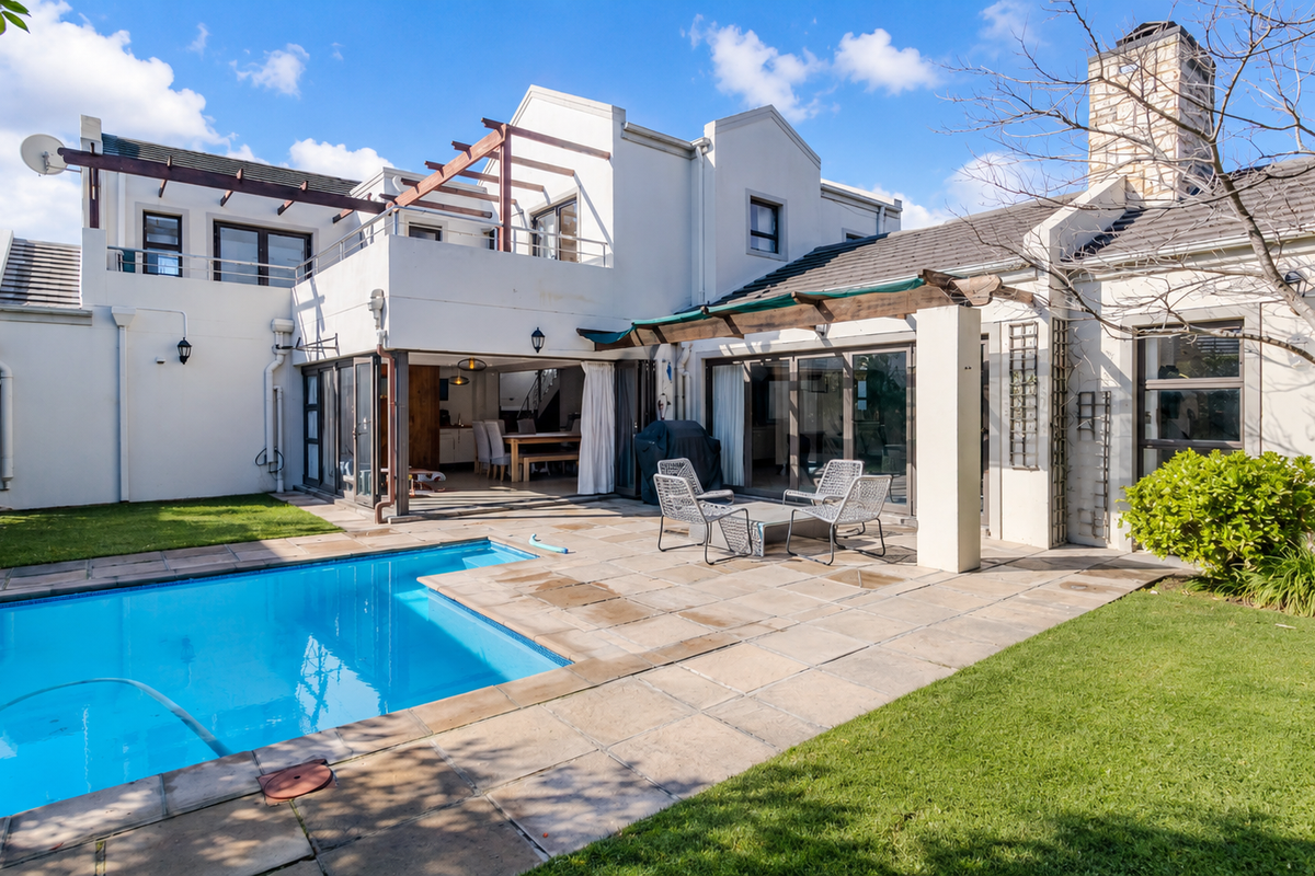 Rear exterior view featuring a swimming pool, stone paved patio, timber pergola, and a balcony overlooking the garden.