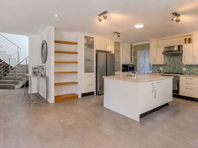 Spacious open-plan kitchen featuring a central island, modern cabinetry, mosaic backsplash, and an adjacent staircase with a contemporary stainless steel balustrade.
