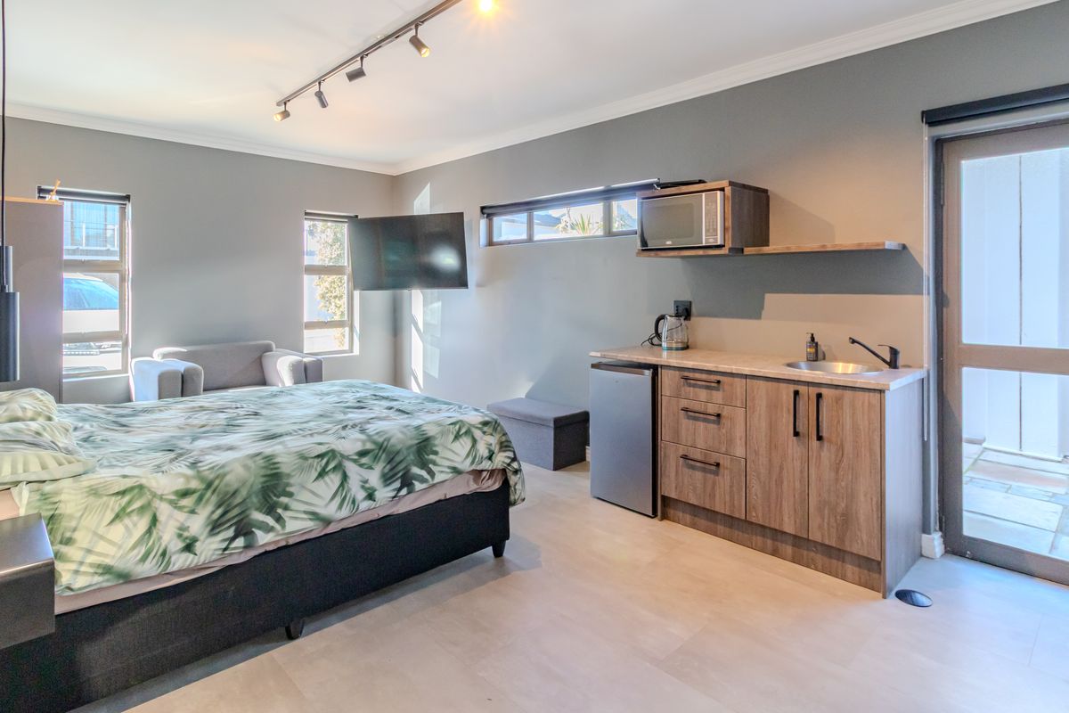 A modern bedroom featuring a convenient kitchenette with built-in cabinetry, sink, and microwave, with direct access to an outdoor area through a glass door.