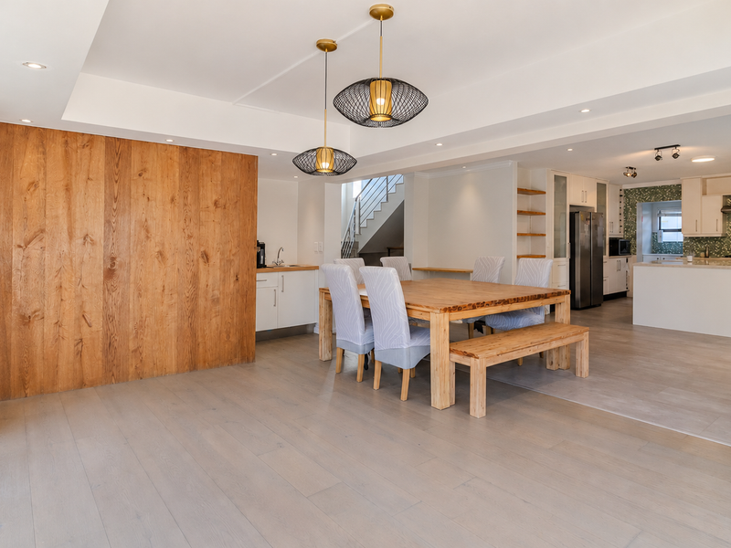 Spacious open-plan living and dining area featuring modern kitchen cabinetry, a central island, timber feature wall, and seamless access to outdoor space.
