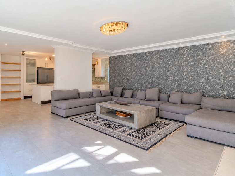Spacious open-plan living area featuring tiled floors, decorative wallpaper, recessed lighting, and a seamless transition to the kitchen and staircase.