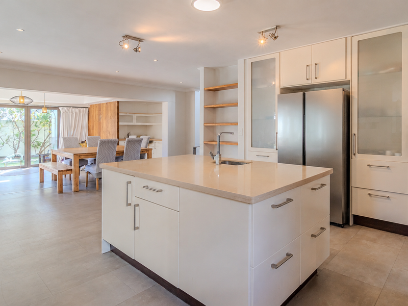 Spacious open-plan kitchen and dining area featuring a central island, modern cabinetry, stone countertops, and seamless access to the outdoor patio through sliding doors.