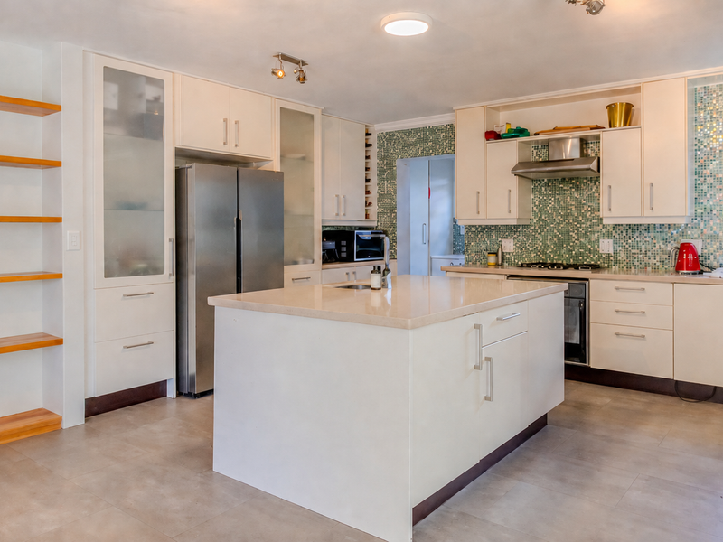 Modern kitchen featuring a central island, stone countertops, ample built-in cabinetry, and a decorative mosaic tile backsplash.