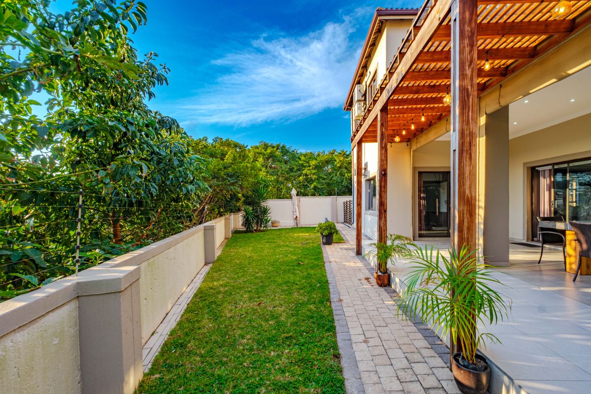 A well-maintained rear garden featuring a paved walkway, a timber pergola over a tiled patio, and secure boundary walls with electric fencing.
