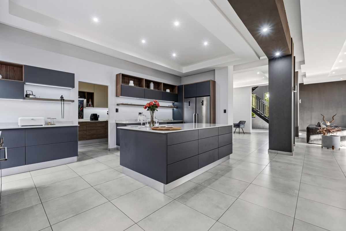 Modern open-plan kitchen featuring a large central island, sleek dark cabinetry, quartz countertops, and high-end integrated appliances with recessed lighting.
