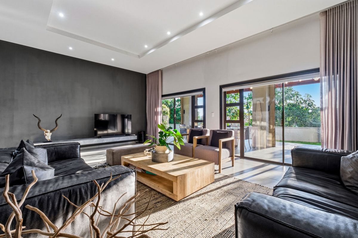Spacious modern living room featuring high ceilings with recessed lighting, a dark feature wall, and large sliding glass doors opening to an outdoor patio.