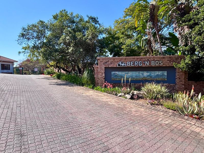 The entrance to Berg 'n Bos estate featuring a brick paved driveway, landscaped gardens, and a decorative brick boundary wall with signage.