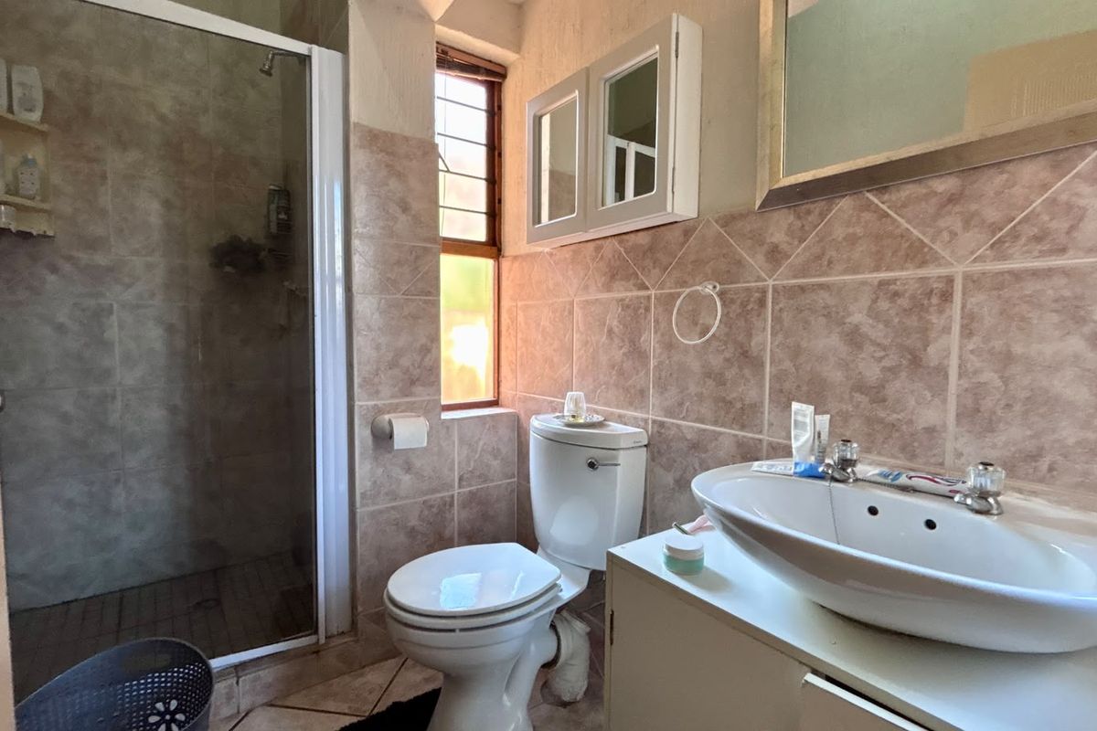 A functional bathroom featuring a shower enclosure, toilet, and vanity basin with wall-mounted storage, finished with neutral-toned wall and floor tiles.