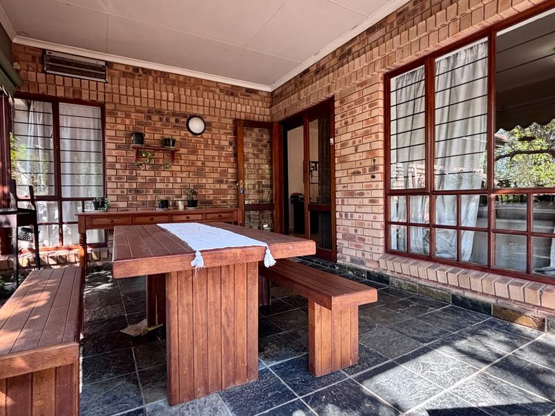 A covered patio area featuring exposed brick walls, slate tile flooring, and large glass windows, providing a functional outdoor entertainment space.