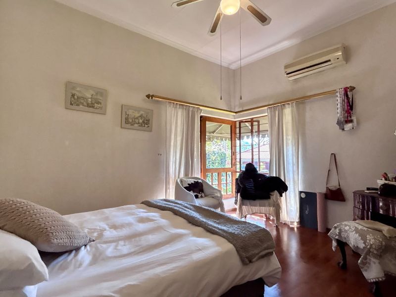A bedroom featuring hardwood flooring, a ceiling fan, a split-system air conditioner, and access to an outdoor area through wooden french doors.