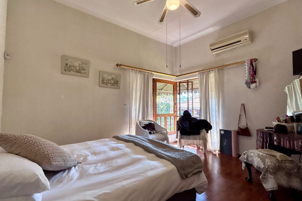 A bedroom featuring hardwood flooring, a ceiling fan, a split-system air conditioner, and access to an outdoor area through wooden french doors.