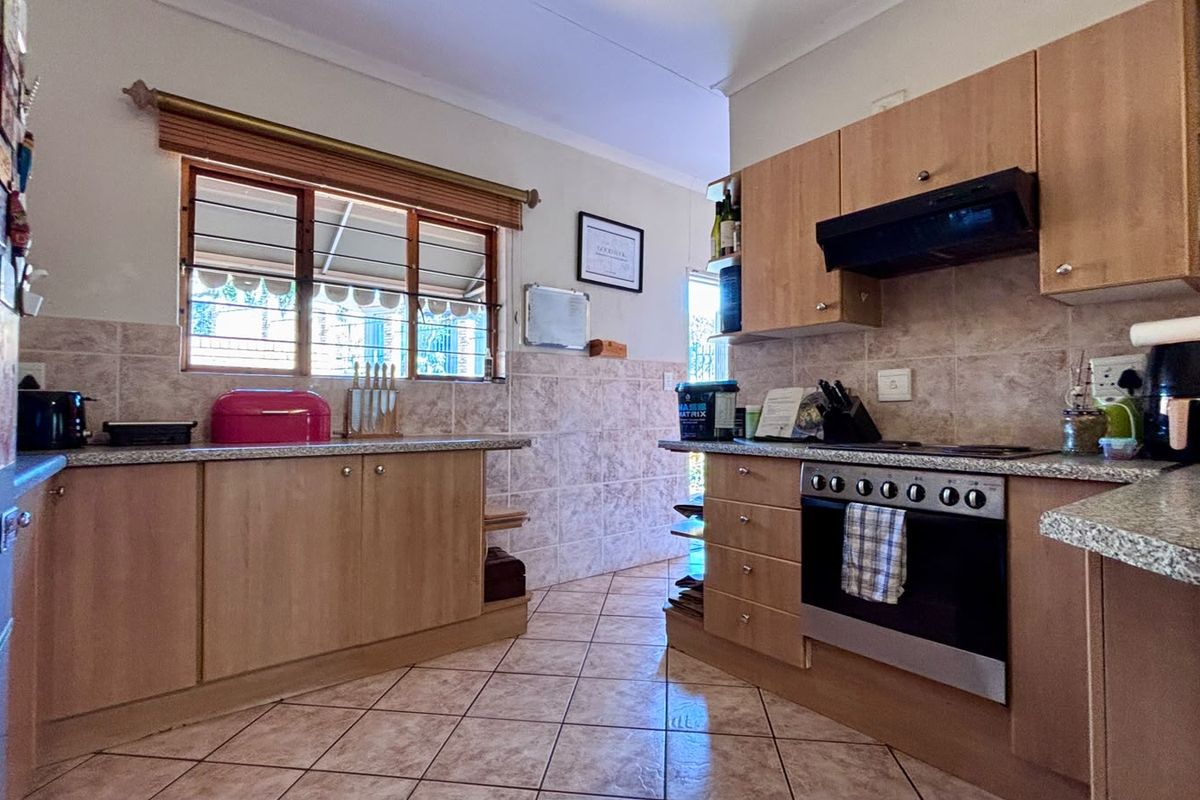 A functional kitchen featuring light wood-finish cabinetry, granite-look laminate countertops, tiled backsplash, and a built-in oven with an extractor fan.