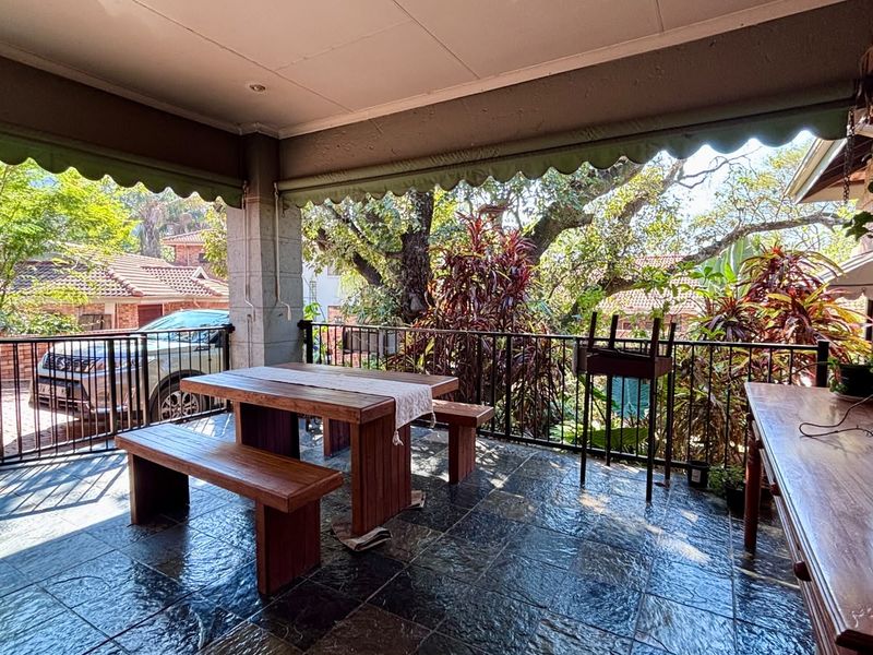 A spacious covered patio featuring durable tiled flooring, a metal balustrade, and a retractable awning, overlooking the garden area.