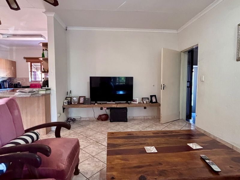 Open plan living area featuring tiled flooring, coved cornicing, and a built-in wall shelf, with an adjacent kitchen area visible in the background.