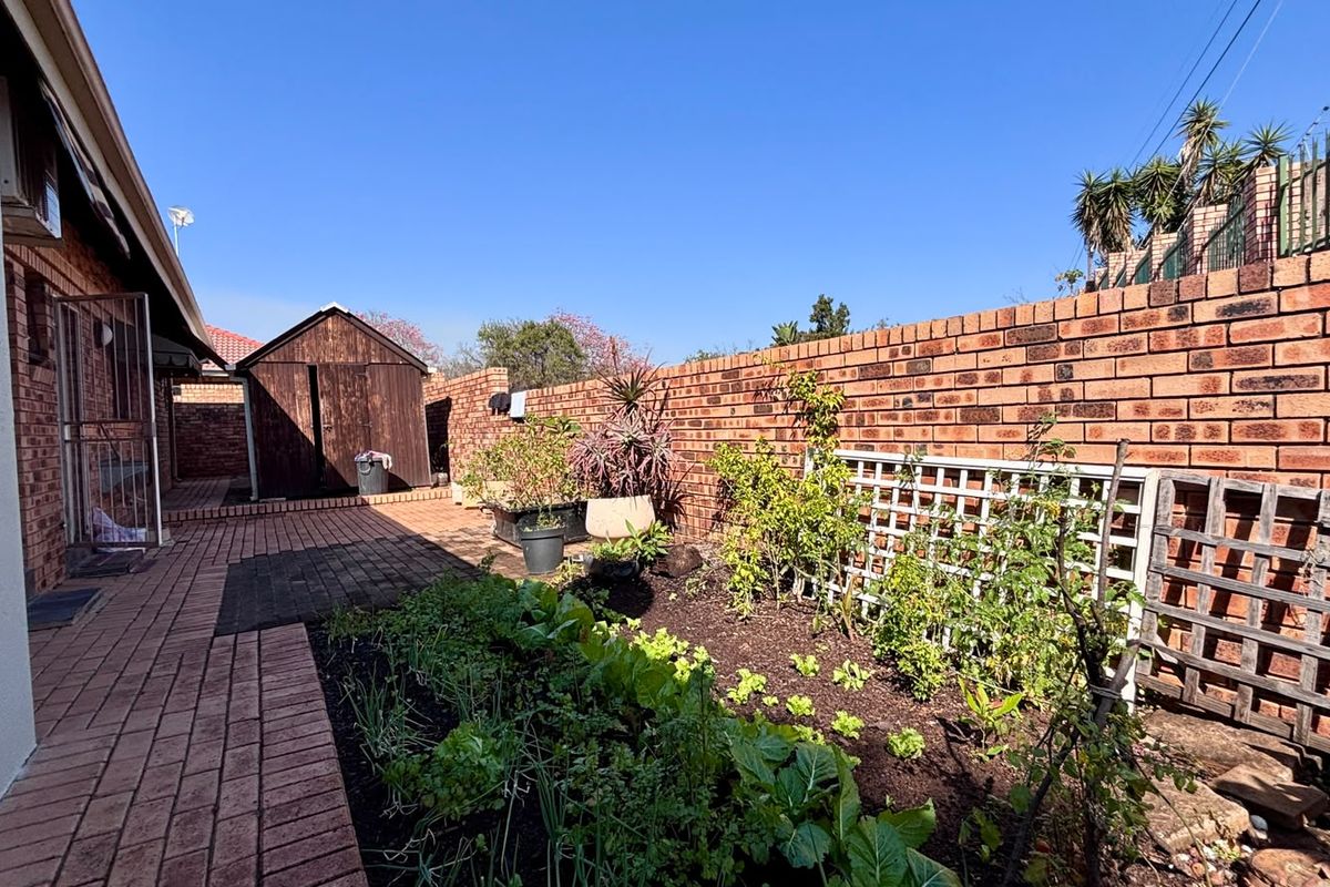 A rear exterior area featuring brick paving, a garden bed with trellis, and a wooden storage shed enclosed by a brick boundary wall.
