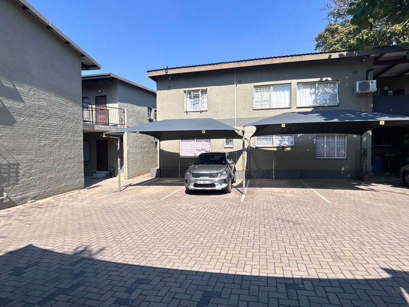 Exterior view of an apartment complex featuring a paved parking area with dedicated shade cloth carports and secure building access.