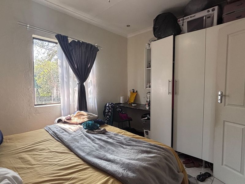 A functional bedroom featuring a built-in wardrobe, integrated desk space, and tiled flooring, offering a practical layout for comfortable living.