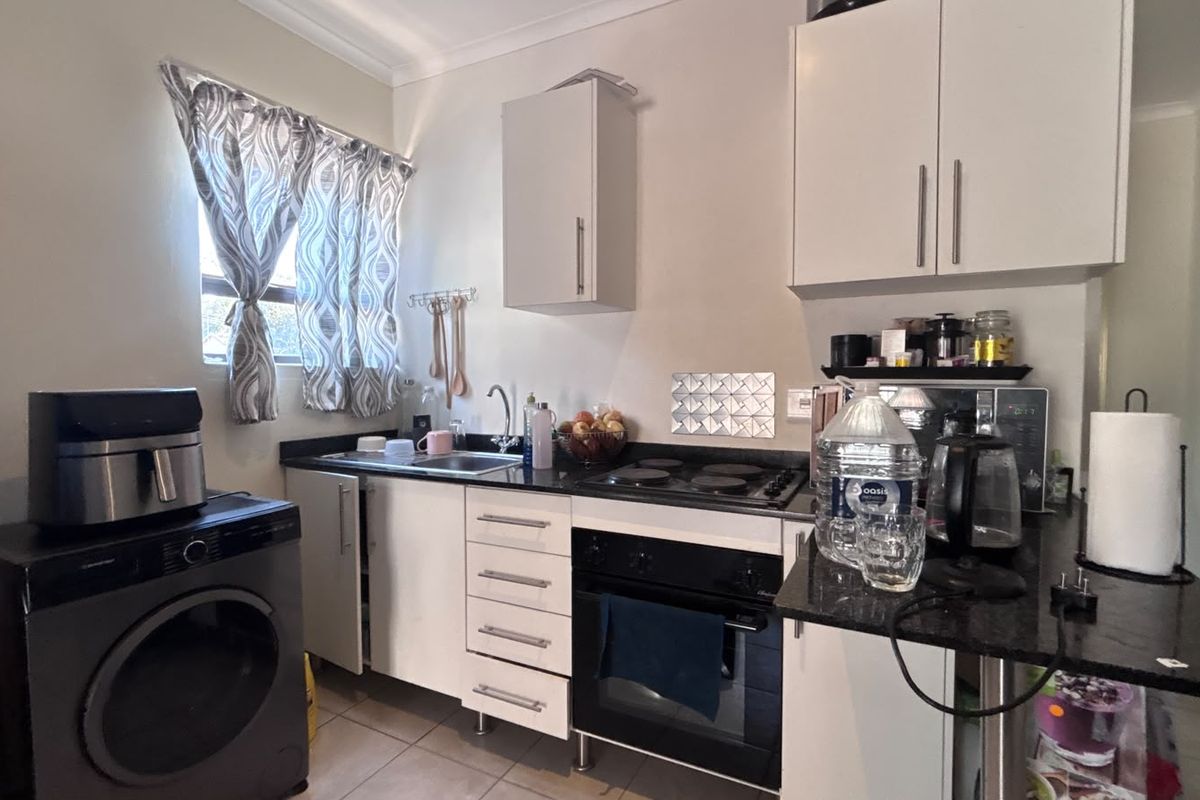 Compact kitchen featuring white cabinetry, granite countertops, built-in oven and hob, and tiled flooring, providing a functional workspace.