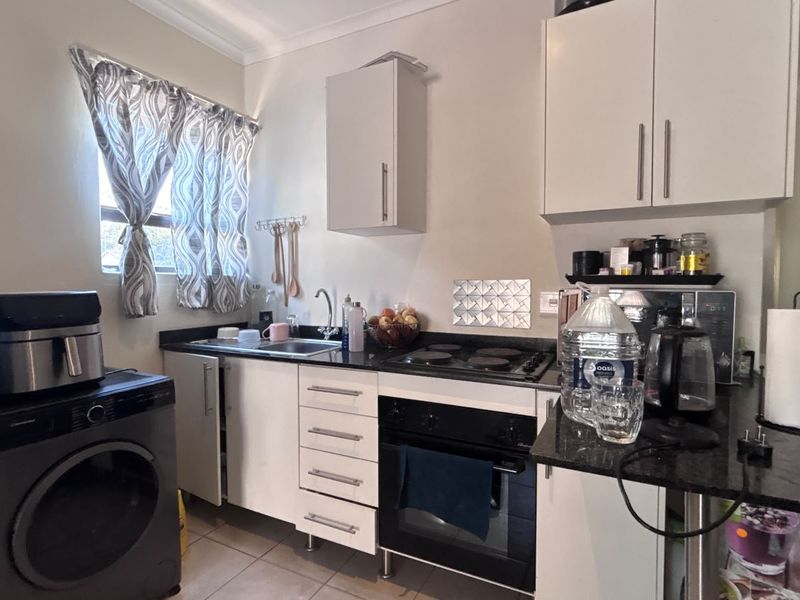 Compact kitchen featuring white cabinetry, granite countertops, built-in oven and hob, and tiled flooring, providing a functional workspace.