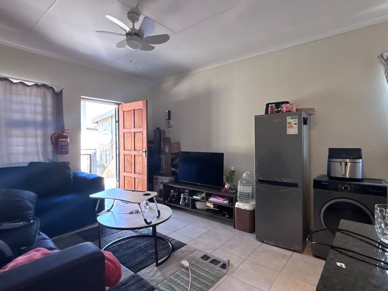 Open-plan living area featuring tiled flooring, a ceiling fan, and direct access to an exterior entrance.