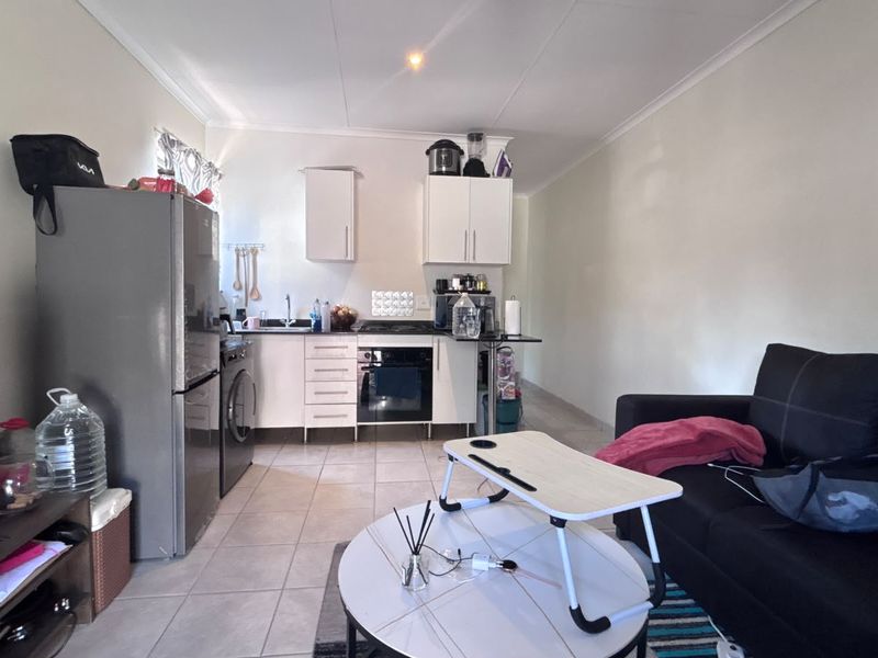 Open-plan living area featuring a compact kitchen with built-in cabinetry, oven, hob, and tiled flooring throughout.