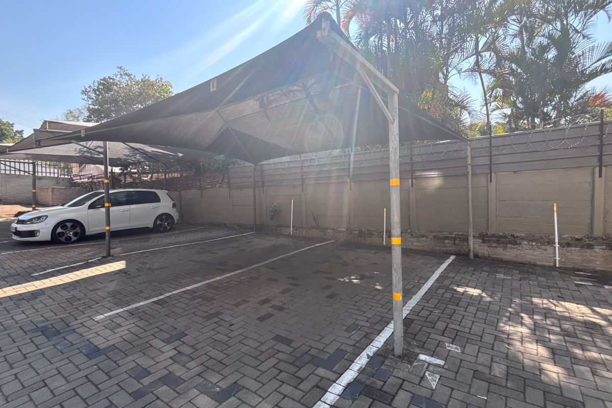 Outdoor paved parking area featuring a shade cloth carport structure and secure perimeter walling with razor wire.