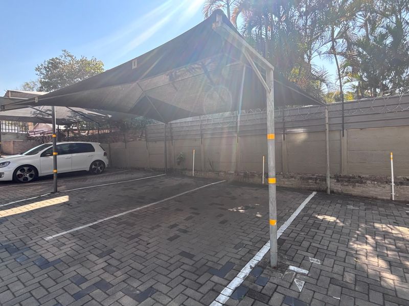 Outdoor paved parking area featuring a shade cloth carport structure and secure perimeter walling with razor wire.
