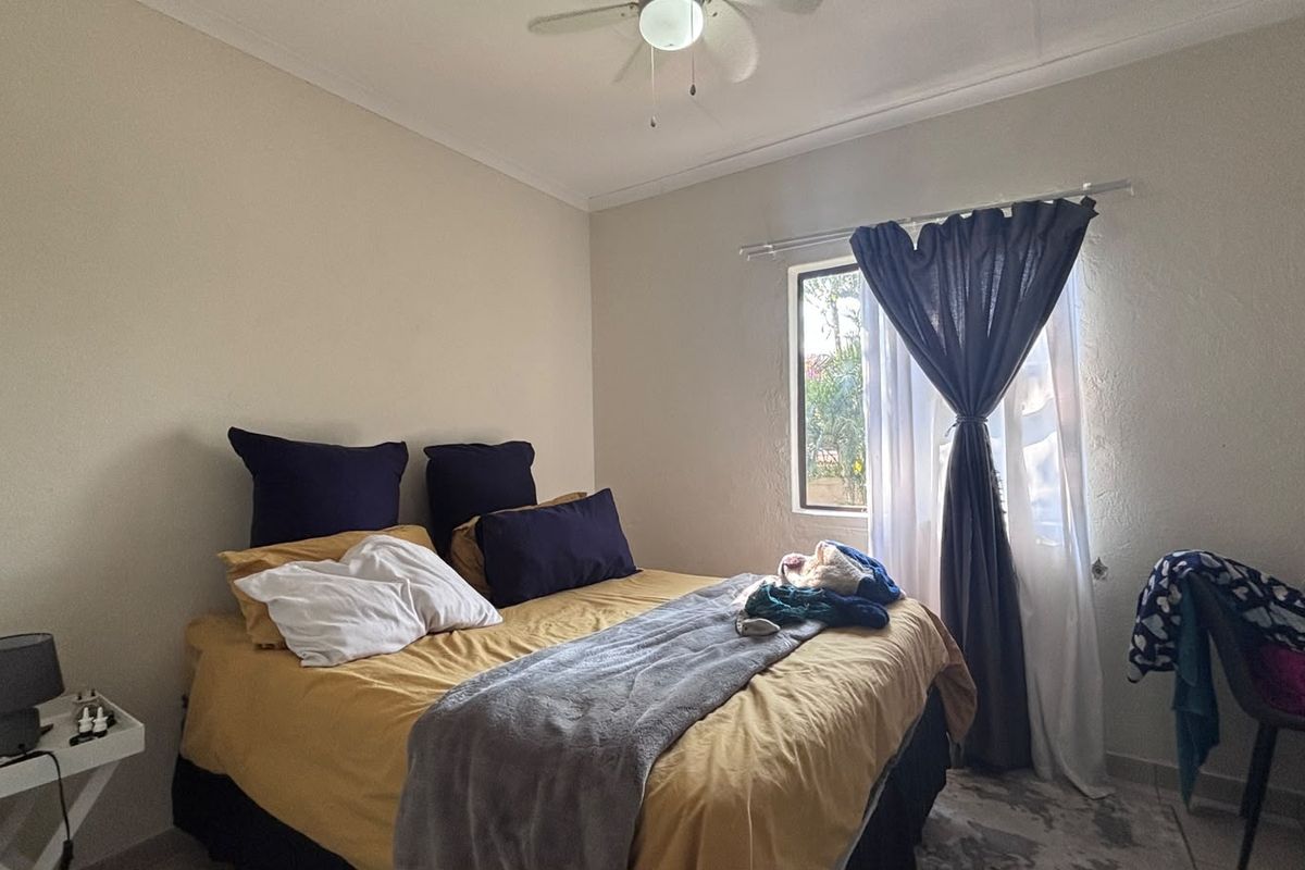 A functional bedroom featuring a ceiling fan and a window with curtain rods, providing natural light and ventilation.