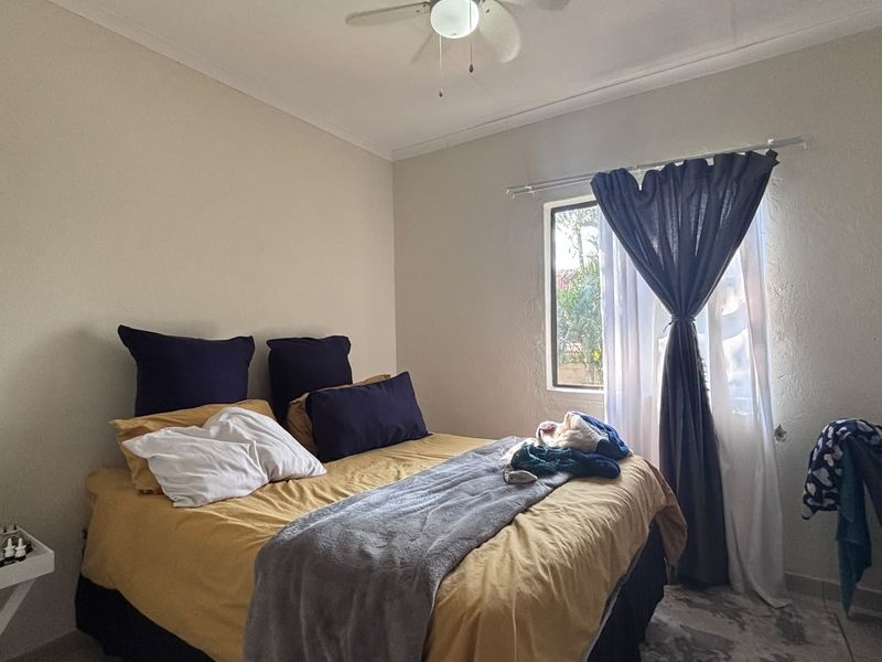 A functional bedroom featuring a ceiling fan and a window with curtain rods, providing natural light and ventilation.