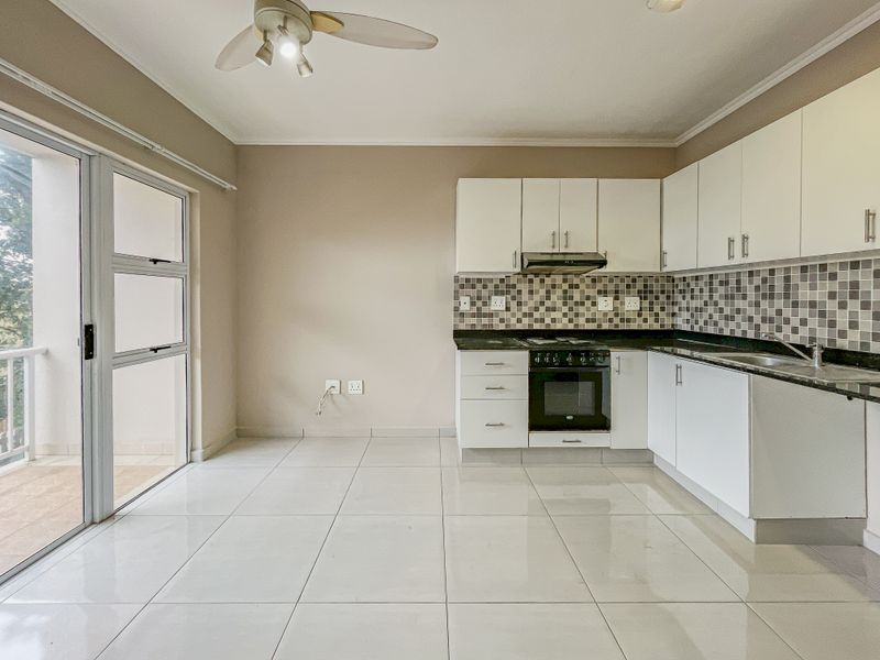Open-plan kitchen featuring white cabinetry, black granite countertops, mosaic backsplash, and tiled flooring, with direct access to a balcony through sliding glass doors.